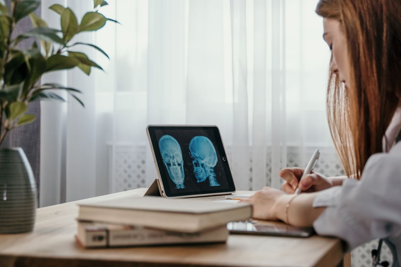 services-03 Doctor in office reviewing skull X-ray on tablet, taking notes for diagnosis.