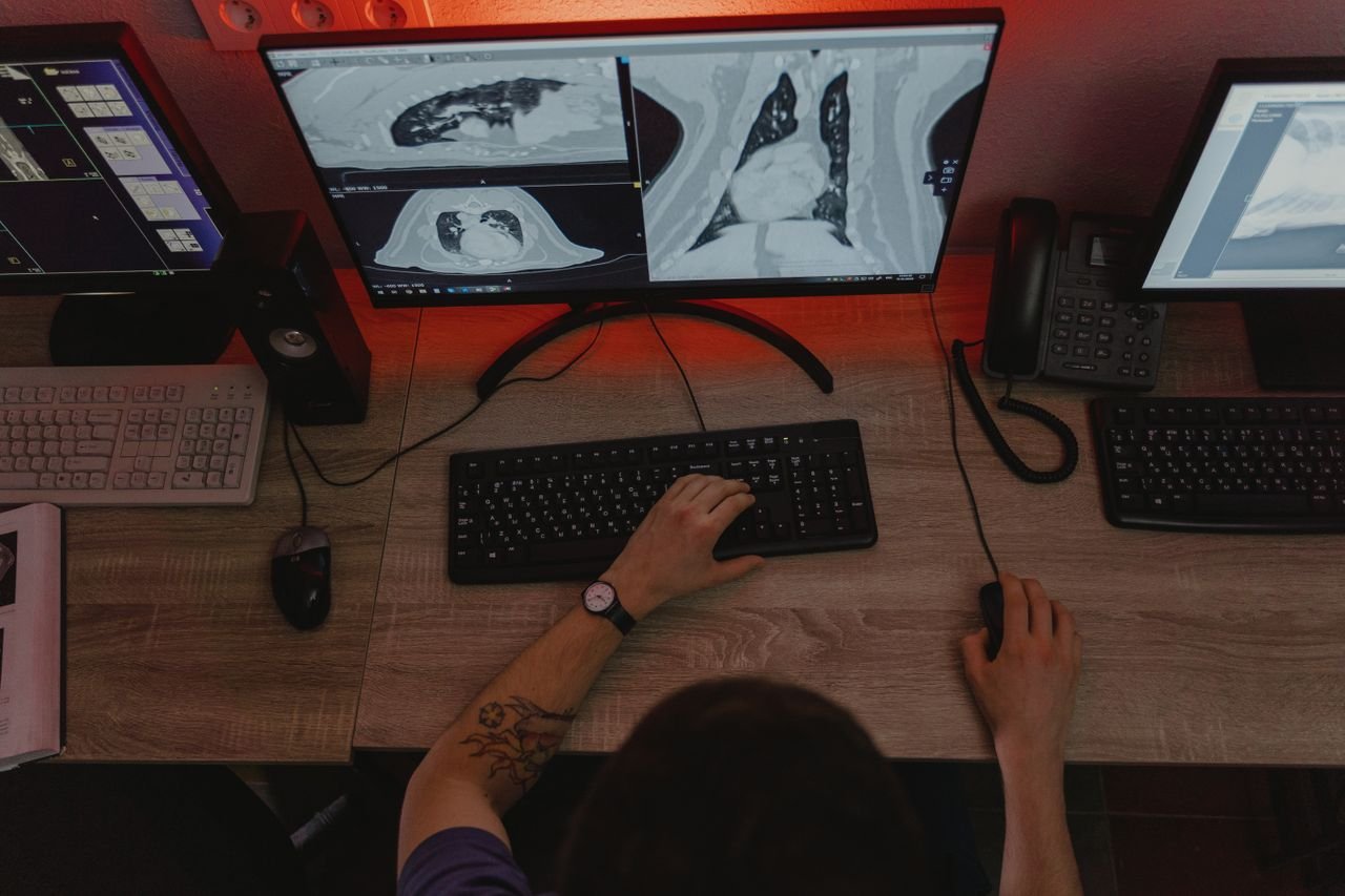 services-02 A radiologist reviews x-ray scans on multiple monitors at a desk, focusing on medical diagnostics.